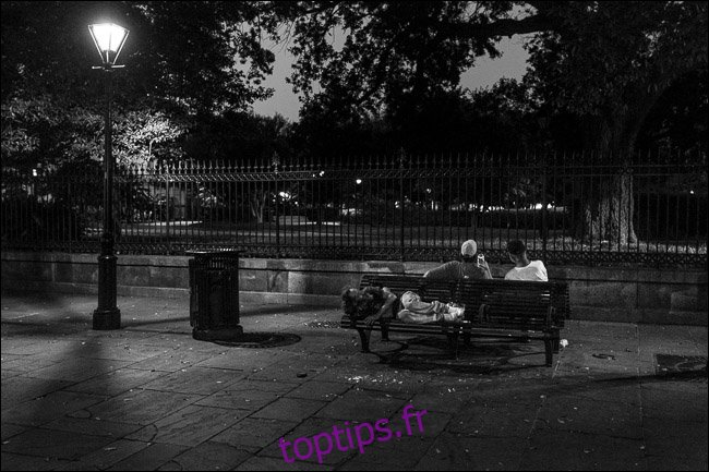 deux hommes assis sur un banc de parc la nuit; un homme dormant sur un siège derrière eux