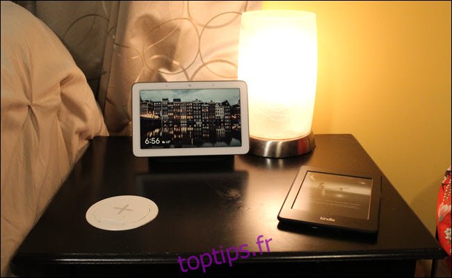 Une table de chevet avec un chargeur sans fil placé dans la surface, un Kindle et Google Home Hub