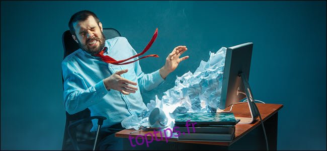 Jeune homme d'affaires beau stressé travaillant au bureau dans un bureau moderne criant à l'écran d'un ordinateur portable et en colère contre le spam par e-mail. Collage avec une montagne de papier froissé.
