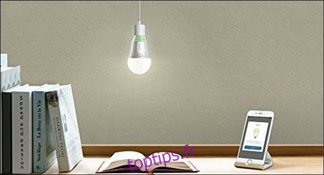 Une ampoule Wi-Fi TP-Link suspendue au-dessus d'un livre ouvert et d'un téléphone portable sur un bureau.