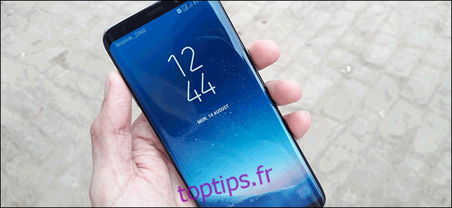 Une main tenant un Samsung Galaxy S8 avec l'écran tactile sur l'affichage de l'heure et de la date.