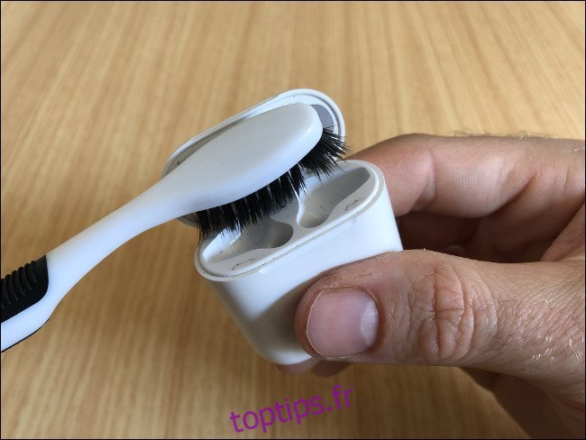 La main d'un homme tenant un étui de chargement AirPods et le nettoyant avec une brosse à dents.