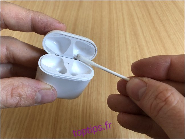 Les mains d'un homme tenant un étui de chargement AirPods et un Q-tip.