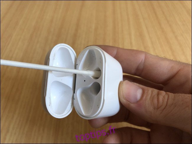 La main d'un homme tenant un boîtier de charge AirPods et nettoyant les canaux de charge avec un coton-tige.