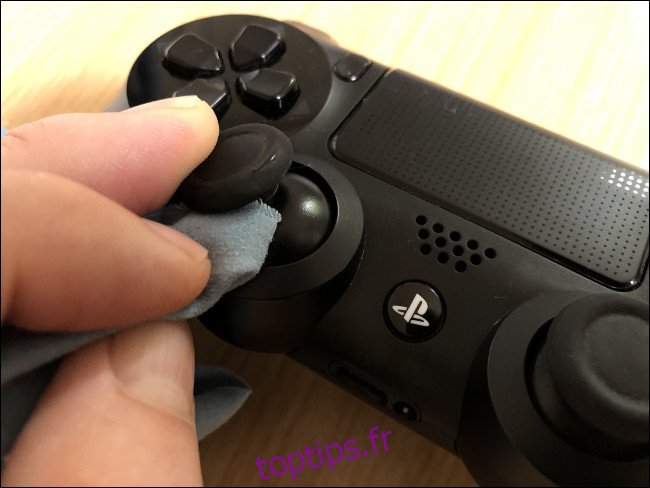 Une main nettoyant une clé analogique avec un chiffon sur un contrôleur DualShock 4.