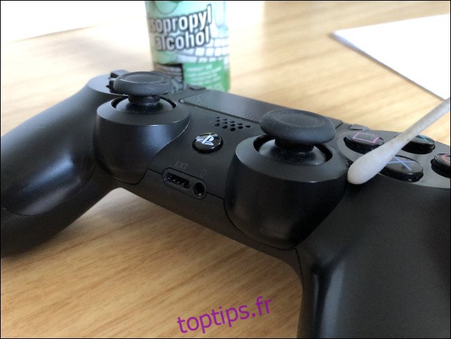 Un contrôleur DualShock 4 avec un Q-tip sur le dessus à côté d'une bouteille d'alcool isopropylique.