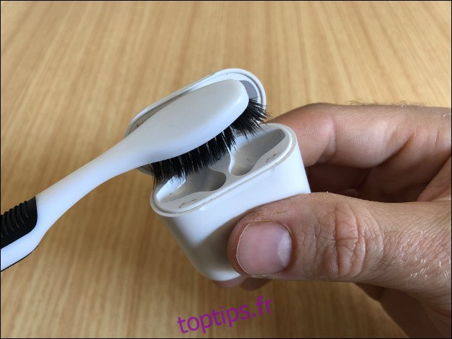 Une main tenant un étui Apple AirPods et le nettoyant avec une brosse à dents.
