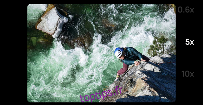 Plan en zoom d'un homme sur une corde escaladant les rochers à côté d'une rivière. 