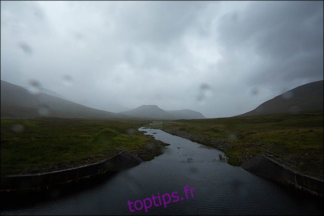 Une photo pluvieuse d'une montagne et d'un ruisseau avec des gouttelettes d'eau sur l'objectif. 