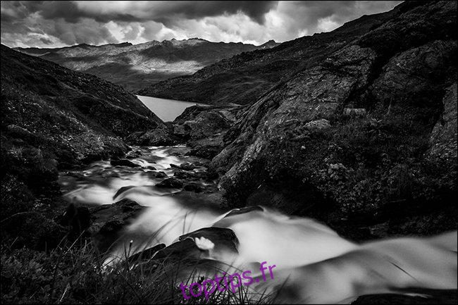 Une photo en noir et blanc d'un ruisseau dans les montagnes après la pluie.