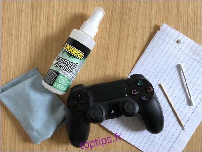 Un contrôleur DualShock 4 posé sur un morceau de papier à côté d'un cure-dent, d'un coton-tige, d'un vaporisateur d'alcool isopropylique et d'un chiffon. 