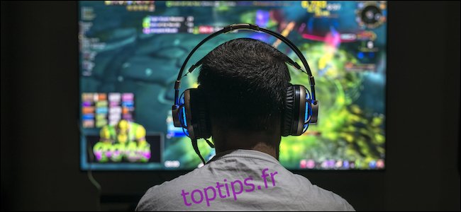 Un homme jouant à des jeux vidéo sur un écran ultra-large, tout en portant des écouteurs.