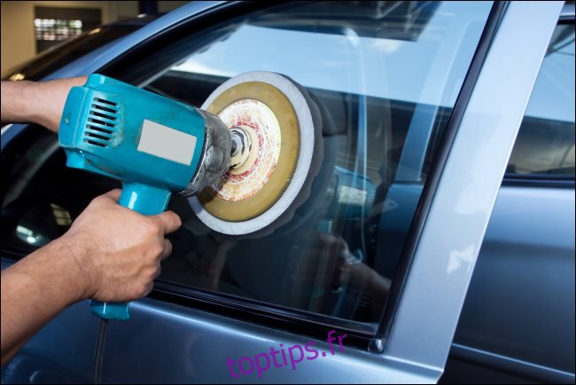 Les mains d'un homme polissant une vitre de voiture avec une machine tampon de puissance.