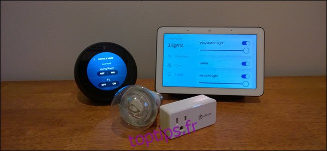 Un Echo Spot, Google Home, une ampoule intelligente et une prise intelligente sur une surface en bois.