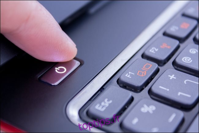 Un doigt appuyant sur le bouton d'alimentation d'un ordinateur portable pour l'éteindre.