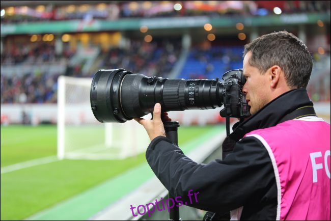 Un photographe avec un grand zoom optique lors d'un match de football.
